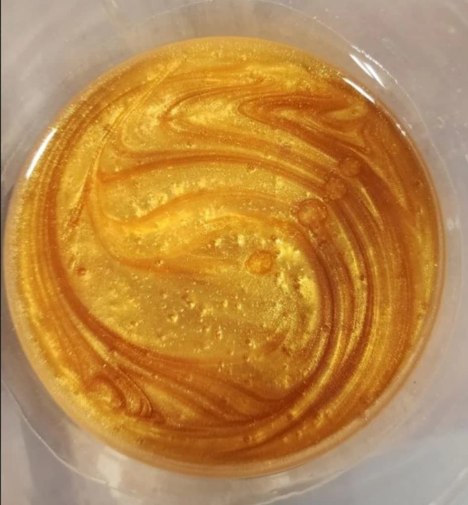 Liquid epoxy resin swirled with metallic gold mica pigment.