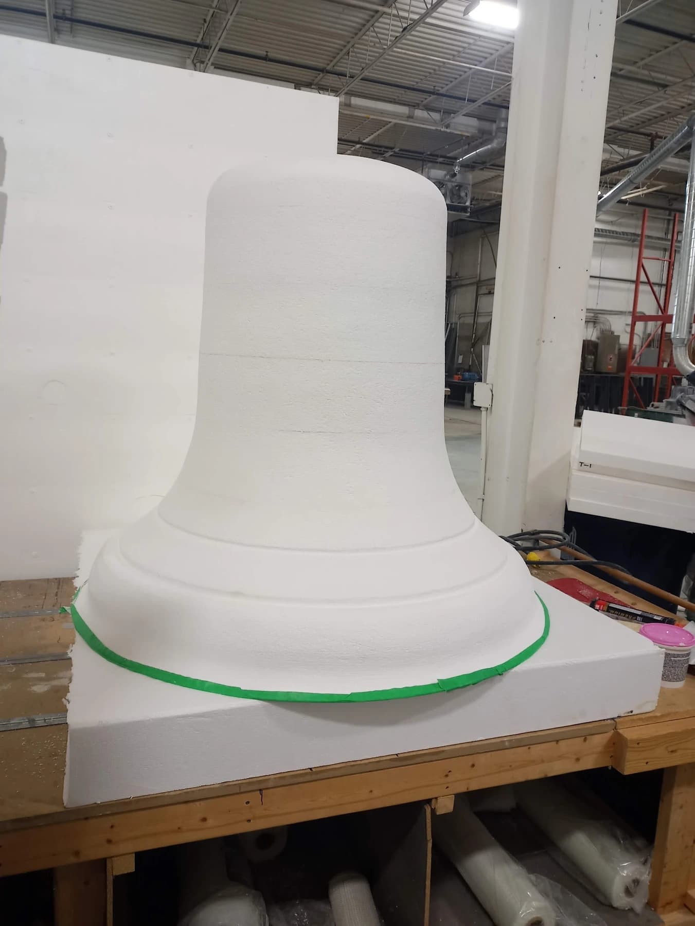 Large white foam bell form on a workshop bench with a flared rim and shaped bands.
